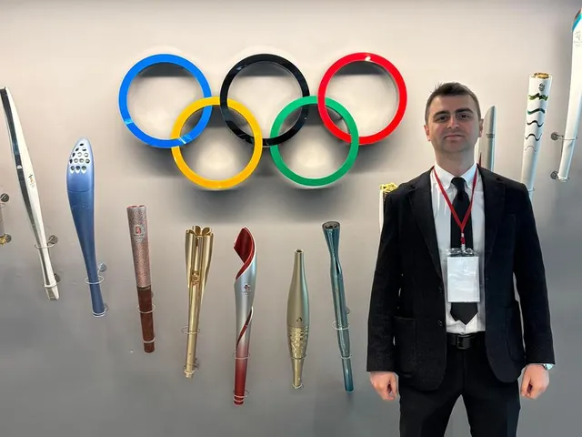Dr. Mehmet Kaymakoğlu standing in front of Olympic rings and torches
